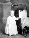 Box 34, Neg. No. 9158: Baby Standing Next to a Stroller