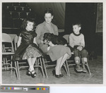 A Woman, Two Children, and a Dog Sitting in Metal Folding Chairs in Sheridan Coliseum at Fort Hays State College 1950s
